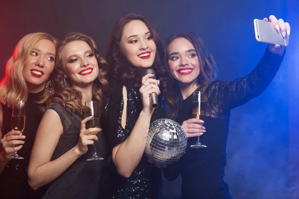 Fiatal nők luxus fekete ruhák pezsgőt iszik, és szórakozás karaoke, szelfi és boldog idő. — Stock Fotó