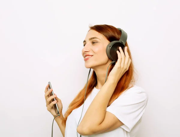 Style de vie et concept de personnes : jeune femme rousse avec écouteurs écoutant de la musique. — Photo