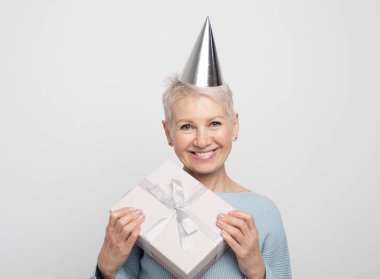 Neşeli, pozitif, mutlu, mavi kazak giyen, parti şapkası takan, beyaz gri arka planda izole tatil havasının tadını çıkaran yaşlı kadının portresi..