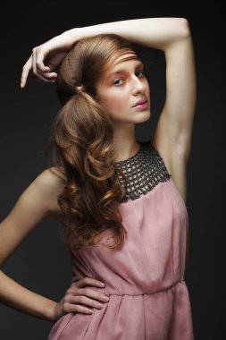 Sarışın, uzun ve gür dalgalı saçlı bir kadın model. Kıvırcık saçlı, siyah arka planda pembe elbiseli bir kadın..