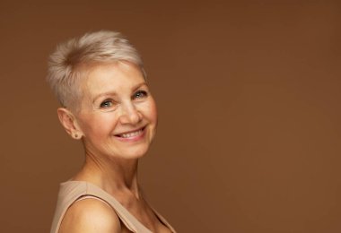 Krem, merhem, maske, losyon, kahverengi arka planda izole edilmiş mükemmel cilde sahip çekici yaşlı bir kadın. Kapat, boşluğu kopyala.