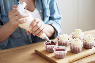 Yemek pişirme, Ev İşleri, Serbest İşletme, İnsanlar ve Hobiler: Sıradan giyinen genç bir kadın keklere beyaz kremayla süsleme yapıyor.