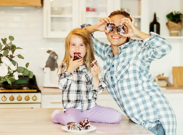 Mor och liten dotter poserar för roliga porträtt kock i köket titta på kameran gör glasögon av kakor. — Stockfoto