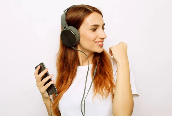 Heureuse jeune femme insouciante dansant et écoutant de la musique depuis son smartphone sur fond gris — Photo