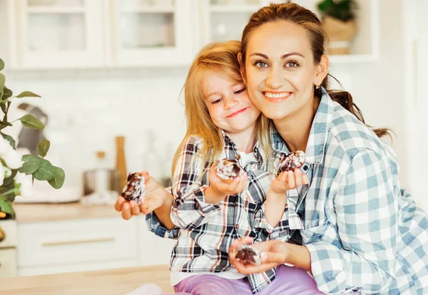 Uma bela jovem mãe e sua filha de quatro anos estão abraçando na cozinha com biscoitos assados. — Fotografia de Stock