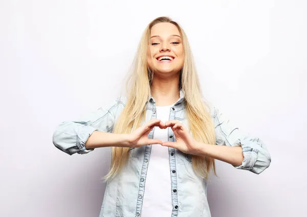 Happy blonde woman shapes heart gesture expresses love smiles pleasantly wears casual has romantic mood — Stock Photo, Image