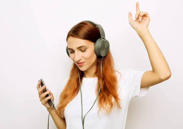 Heureuse jeune femme insouciante dansant et écoutant de la musique depuis son smartphone sur fond gris — Photo
