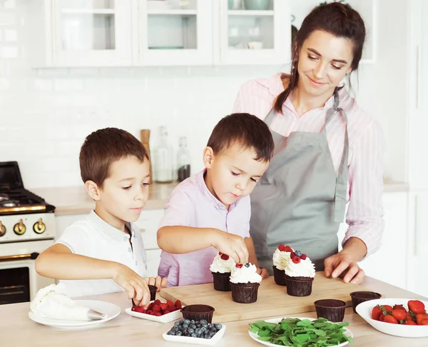 Familia feliz en la cocina. Mamá y dos niños pequeños, hermanos hacen cupcakes caseros. —  Fotos de Stock