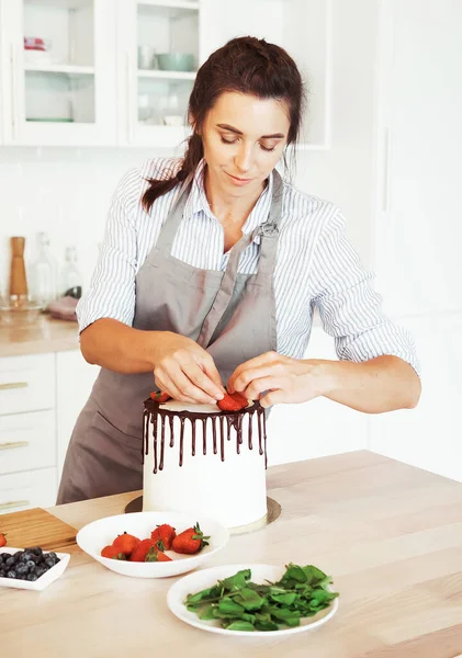 Young woman pastry chef in the kitchen decorating cake with berries and chocolate. — Stock Photo, Image