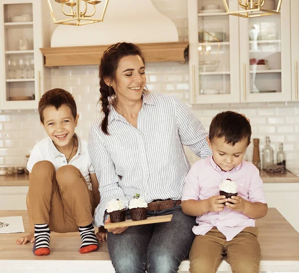 Happy family in the kitchen. Mom and two little boys, brothers, are eating homemade cupcakes. — Stock Photo, Image