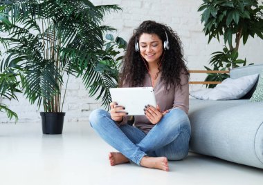 Rahatlamış, melez, gülümseyen, mutlu ve evinde kanepede kitap okuyan genç bir kadın..