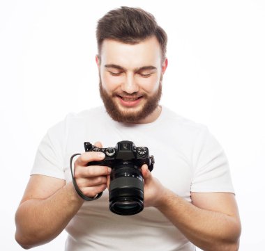 Genç sakallı bir erkek fotoğrafçı beyaz arka planda yalnız başına çektiği fotoğraflara bakıyor..