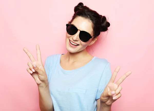 Jong brunette vrouw dragen blauw t-shirt in zonnebril dragen blauw t-shirt tonen overwinning teken over roze achtergrond — Stockfoto