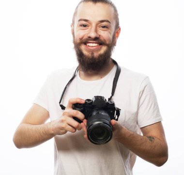 Genç sakallı adam beyaz tişört ve dijital kamera giyiyor.