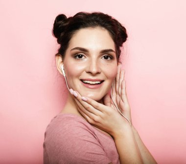 Kulaklıklı güzel esmer kadın pembe arka planda müzik dinliyor.