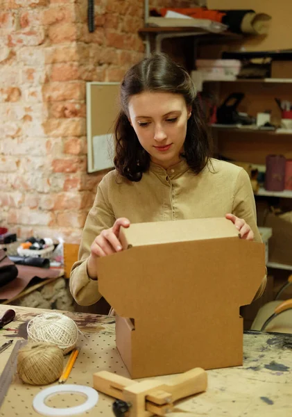 Una giovane donna piega una scatola di cartone per confezionare merci per un cliente. — Foto Stock