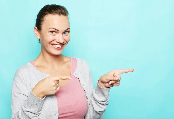Mujer joven sonriente señalando con el dedo el espacio de copia en blanco a un lado —  Fotos de Stock