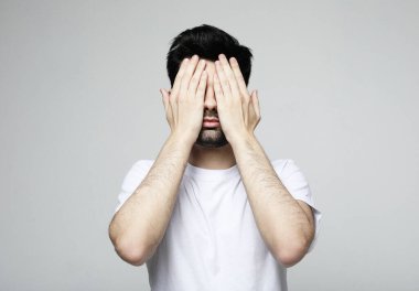 Gri arka planda elleri kapalı genç yakışıklı adam gözlerini kapatıyor.