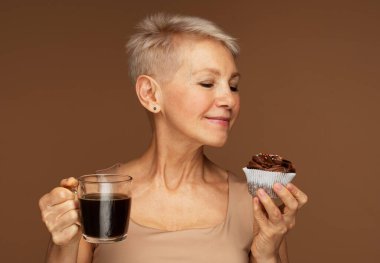 Yaşlılık, yemek, içki ve insanların konsepti - bir fincan kahve ve çikolatalı kekle gülümseyen son sınıf öğrencisi kadın.