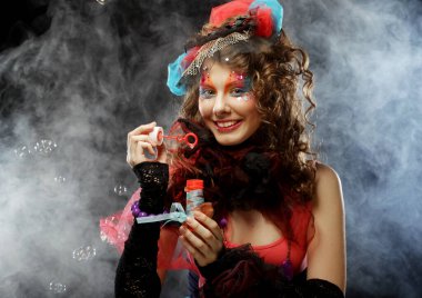 Yaratıcı makyajlı, sabun köpüğü üfleyen modaya uygun genç bir kadın. Bebek stili. Parlak elbise. Siyah arkaplan.