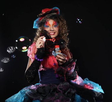 Yaratıcı makyajlı, sabun köpüğü üfleyen modaya uygun genç bir kadın. Bebek stili. Parlak elbise. Siyah arkaplan.