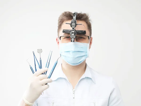 Joven dentista masculino con bata de laboratorio blanca y máscara que sostiene instrumentos dentales —  Fotos de Stock