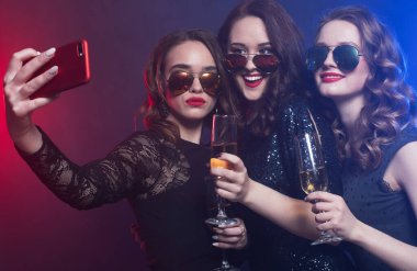 Siyah elbiseli bir grup gülen kadının yakın plan fotoğrafları. Parti veriyorlar, akıllı telefonlu selfie çekiyorlar.