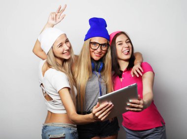 Üç genç bayan arkadaş dijital tabletle selfie çekiyorlar.