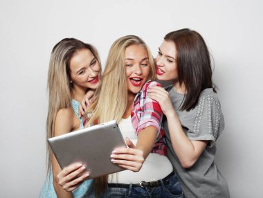 Üç genç bayan arkadaş dijital tabletle selfie çekiyorlar.