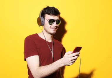 Günlük tişört ve güneş gözlüğü takan genç yakışıklı adam kulaklıkla müzik dinliyor.