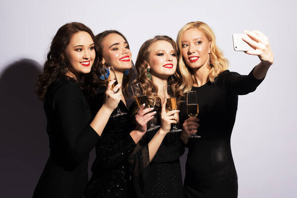 Концепция праздников, вечеринок и людей - четыре модные девушки пьют шампанское и делают селфи