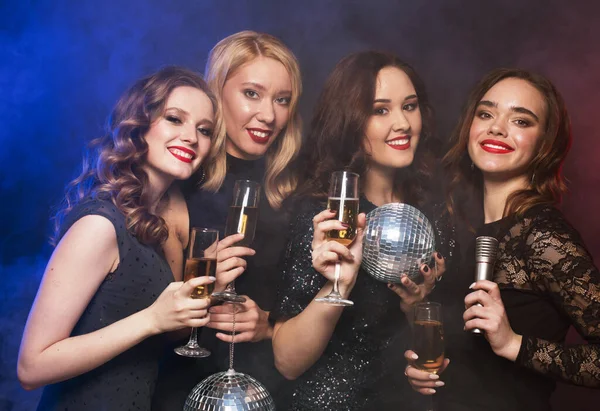 Grupo de mulheres festejando flautas clinking com vinho espumante e segurando bolas de discoteca e microfone. — Fotografia de Stock