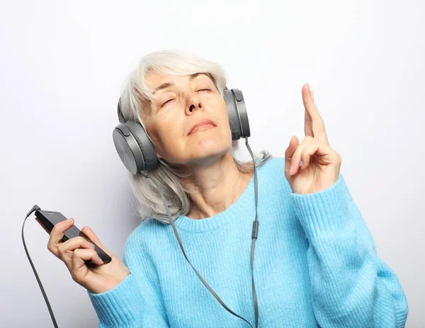 Neşeli yaşlı kadın, beyaz arka planda kulaklıkla müzik dinliyor.