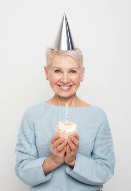 İnsanlar, yaşlanma ve olgunluk kavramı. Doğum gününü kutlayan koni şapkalı, güzel, yaşlı bir kadın elinde mumla yalnız poz veriyor. Mutlu zamanlar..