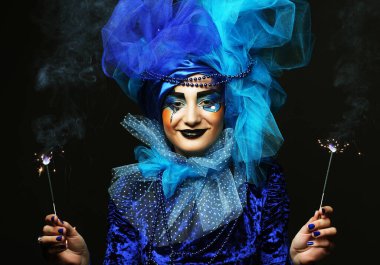 Yaratıcı görünüşlü, kostümlü, siyah arka planda ışıltılar tutan genç ve güzel bir kadın. Parti konsepti.