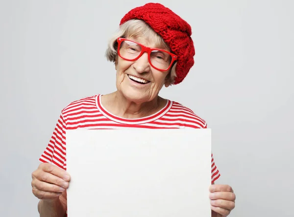 Portret szczęśliwej seniorki z pustą tablicą reklamową lub przestrzenią do kopiowania, na jasnoszarym tle — Zdjęcie stockowe