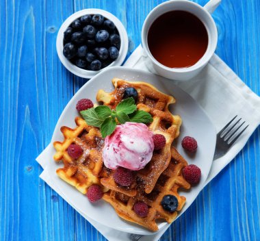 Taze böğürtlenli Belçika waffle 'ları ve mavi ahşap arka planda dondurma.