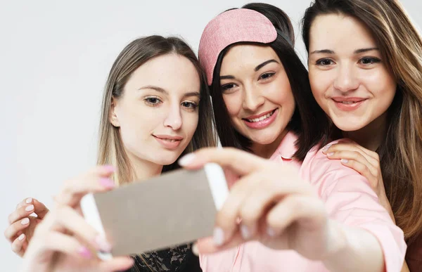 Tre unga kvinnor vänner bär pyjamas med smartphone tar selfie — Stockfoto
