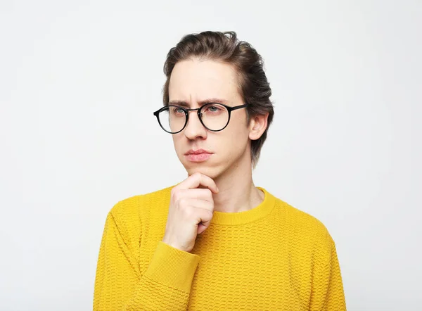 Portret van een slimme jongeman raakt zijn kin, reflecteert, het maken van een beslissing staan tegen witte achtergrond — Stockfoto