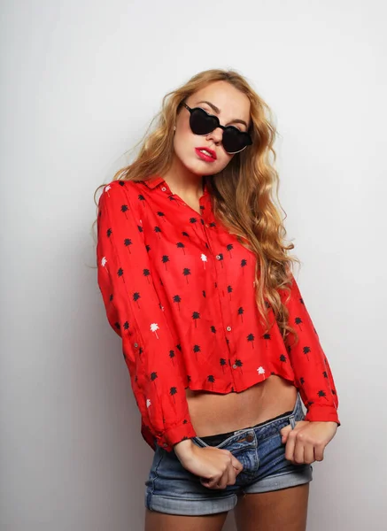 Una giovane donna moderna in camicia rossa e occhiali da sole su sfondo bianco — Foto Stock