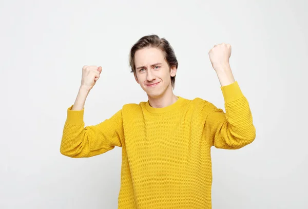 Jonge man draagt gele trui erg blij en enthousiast doen winnaar gebaar met opgeheven armen — Stockfoto