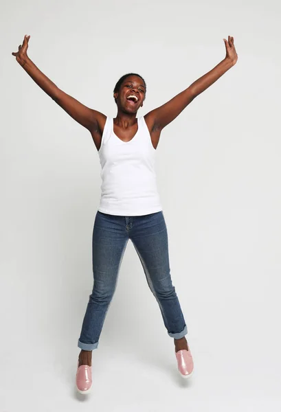 Gri arka planda yalnız atlarken başarıyı kutlayan mutlu Afrikalı genç bir kadın. — Stok fotoğraf