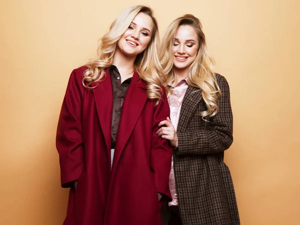 Positivt mode porträtt av två flickor, bästa vänner poserar inomhus på beige bakgrund — Stockfoto