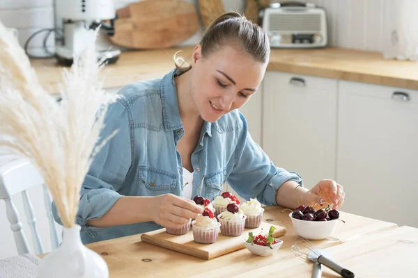 Young woman decorates cupcakes with berries — Stock Photo, Image