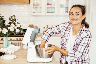 Parlak bir mutfakta dururken yemek makinesinde hamur hazırlayan güzel bir kız.