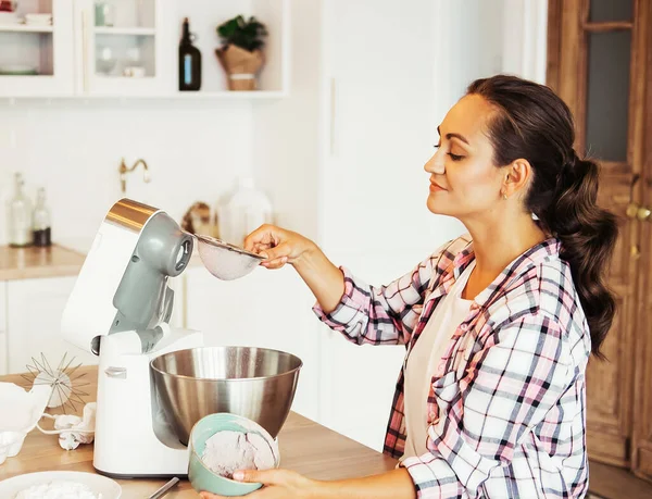 Beautiful girl preparing dough in a food processor while standing in a bright kitchen — Stock Photo, Image