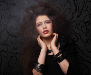 Uzun kıvırcık saçlı, akşam makyajlı, siyah elbiseli ve mücevher takan güzel bir kadın.