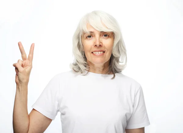 Oude dame draagt witte casual t-shirt met v-teken overwinning vredesgebaar — Stockfoto