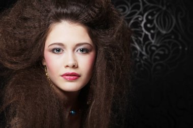 Uzun kıvırcık saçlı, akşam makyajlı, siyah elbiseli ve mücevher takan güzel bir kadın.