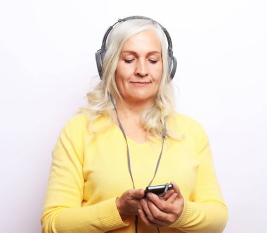 Neşeli yaşlı kadın, beyaz arka planda kulaklıkla müzik dinliyor.